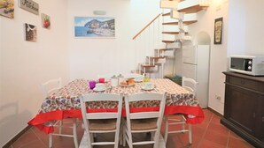 Een eethoek met een tafel voor vier personen, witte stoelen, een rode tafelkleed, en een keuken met een magnetron en een koelkast.