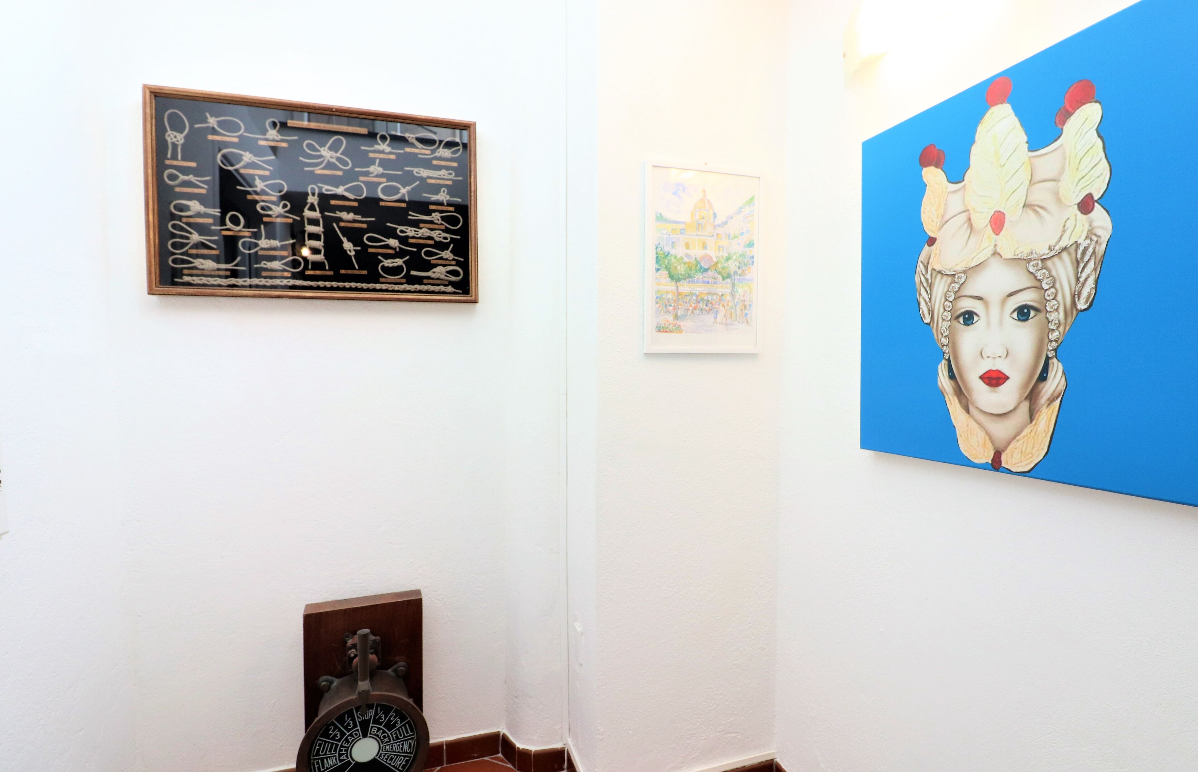A room with a framed artwork of scissors, a framed painting of a building, and a large painting of a woman with a crown.