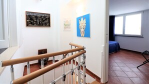 Een trap met houten leuningen en metalen steunpilaren, een muur met ingekaderde kunstwerken, en een raam met een blauw gordijn.