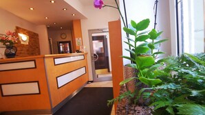 A reception area with a wooden desk, a black mat, and a potted plant. - City Hostel (Augsburg)