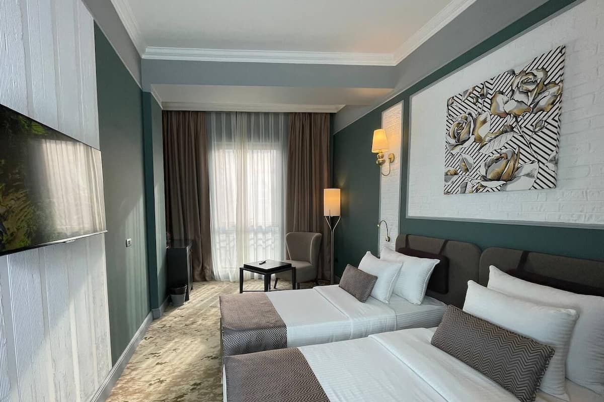 A hotel room with two beds, a desk, a chair, a lamp, and a decorative wall piece.