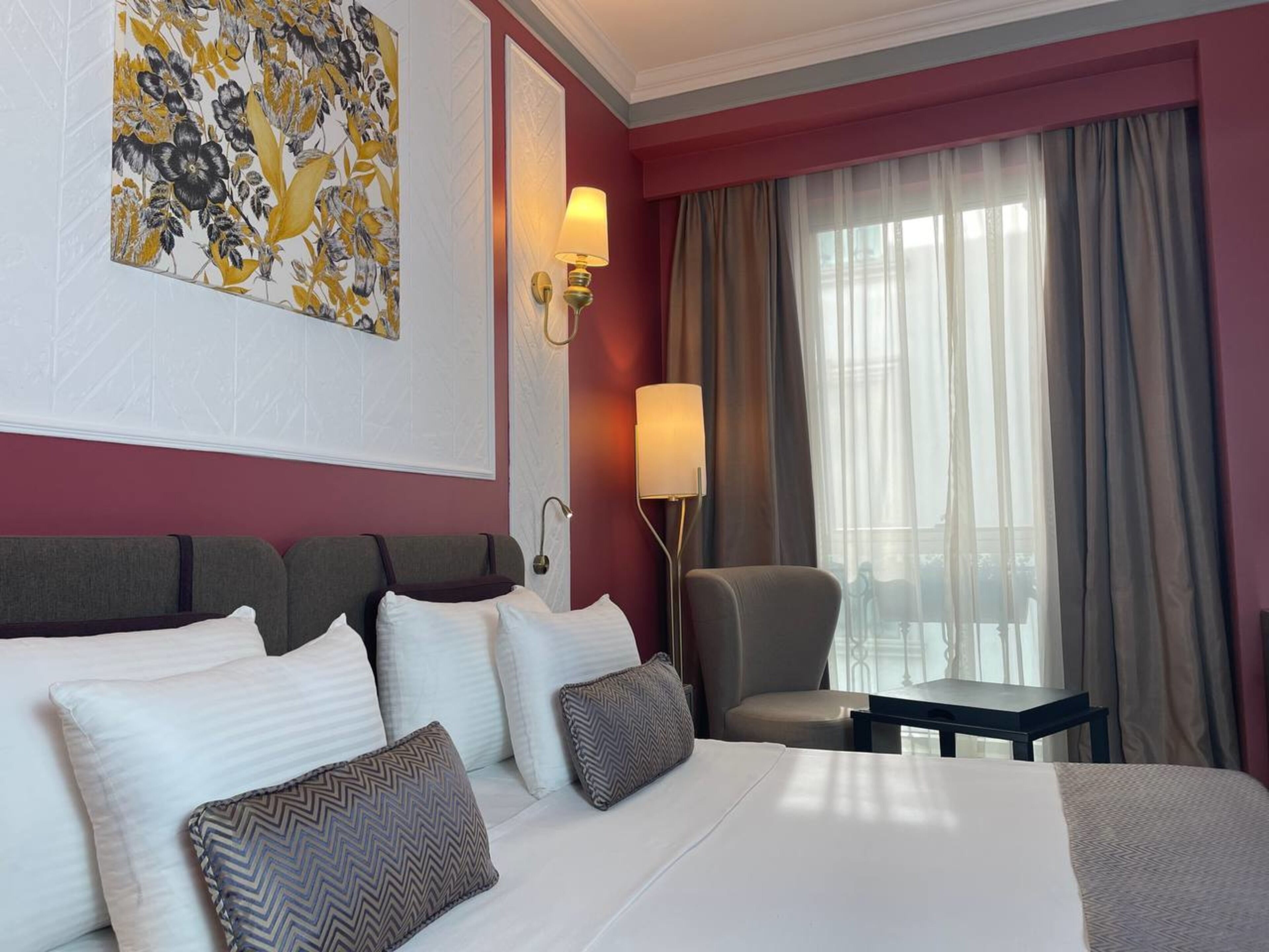 Ein Hotelzimmer mit einem großen Bett, einem Sessel, einem Schreibtisch und einem Fenster mit Vorhängen.