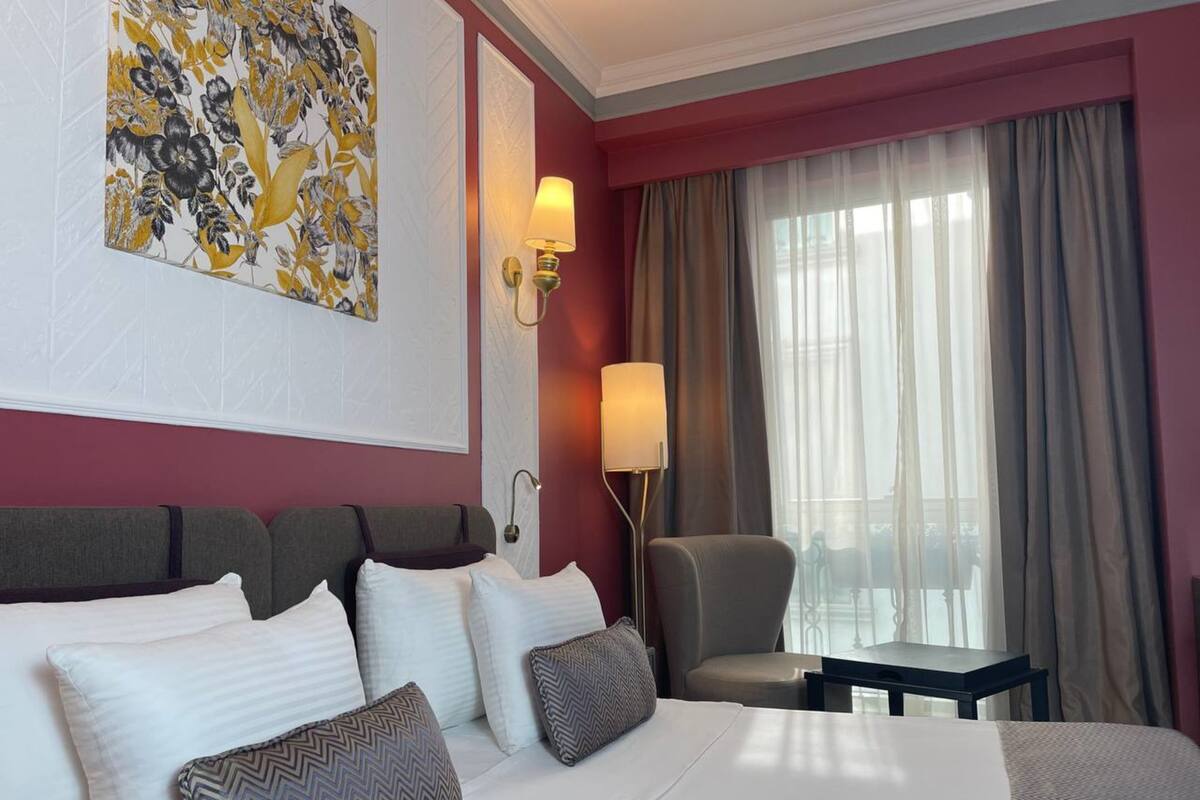 A hotel room with a large bed, a chair, a desk, and a window with curtains.