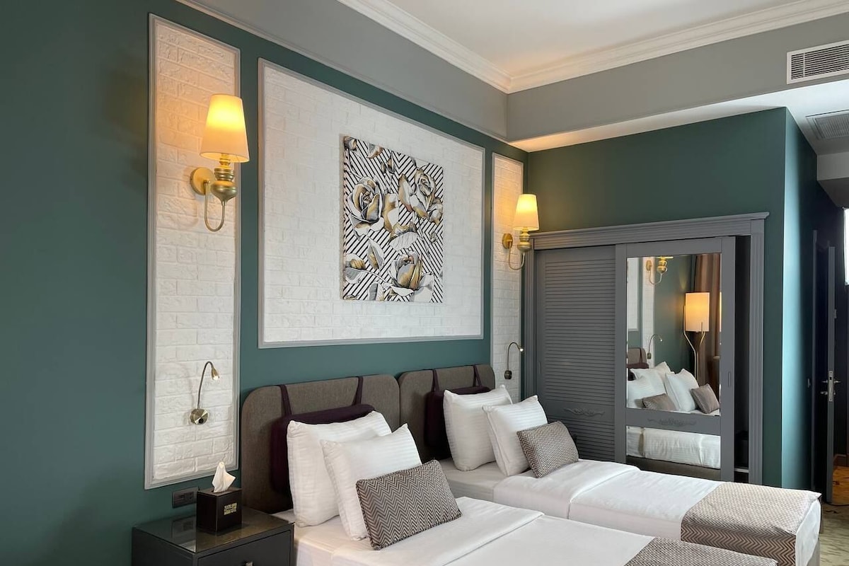 A hotel room with two beds, a large mirror, and artwork on the walls.
