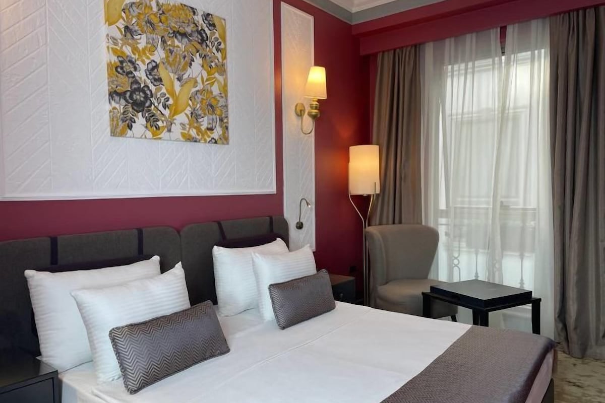 A hotel room with a large bed, a desk, a chair, and a window with curtains.