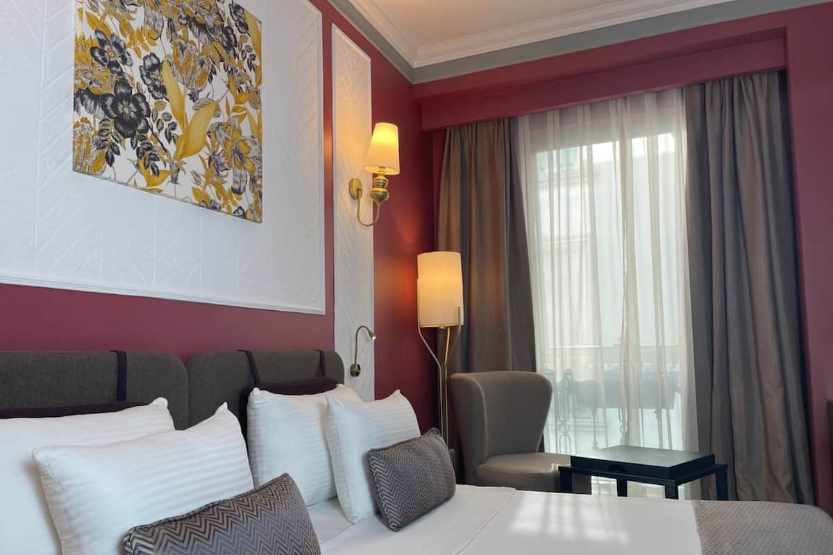 A hotel room with a large bed, a chair, a desk, and a window with curtains.