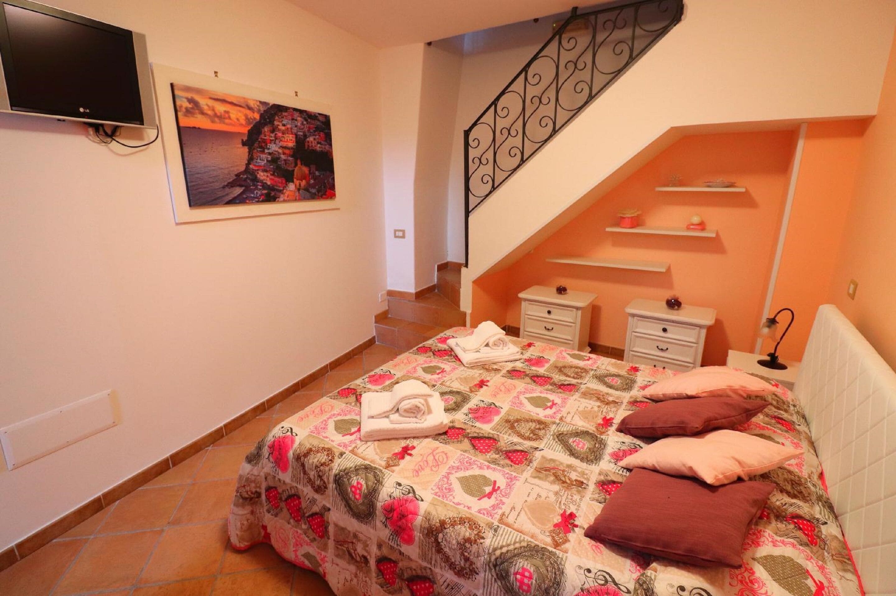 A bedroom with a bed, a TV, a staircase, and a painting on the wall.