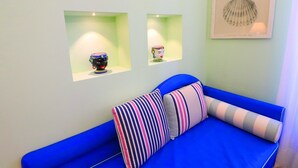 A room with a blue sofa, two wall-mounted shelves with decorative items, and a framed picture on the wall. - Henry House (Sorrento)