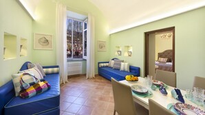 A cozy living room with a blue sofa, a dining table set with plates and glasses, and a window with curtains. - Henry House (Sorrento)