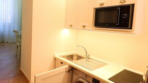 A compact kitchen with a built-in washing machine, a microwave, and a sink. - Henry House (Sorrento)