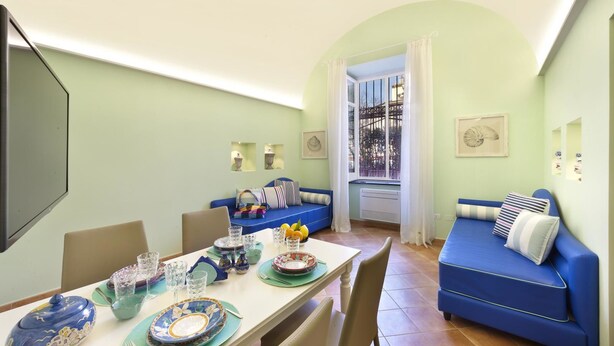 A dining area with a table set for four, a blue sofa, and a window with a view of a balcony. - Henry House (Sorrento)