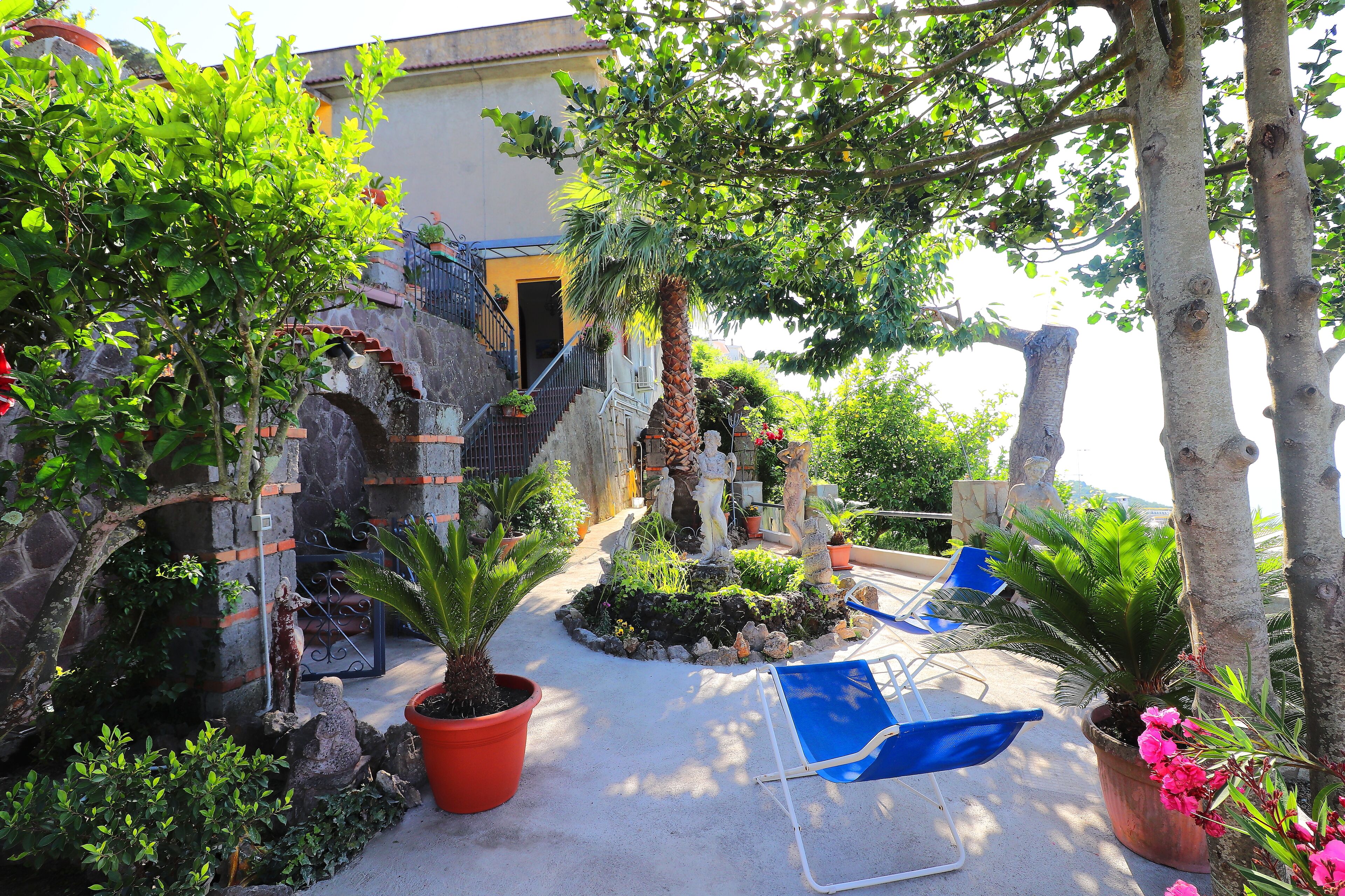 A courtyard with a fountain, potted plants, and a blue chair.