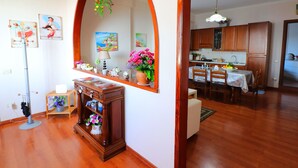 Un soggiorno con pavimento in legno, una zona pranzo con tavolo e sedie, e una cucina con mobili in legno e un lampadario.