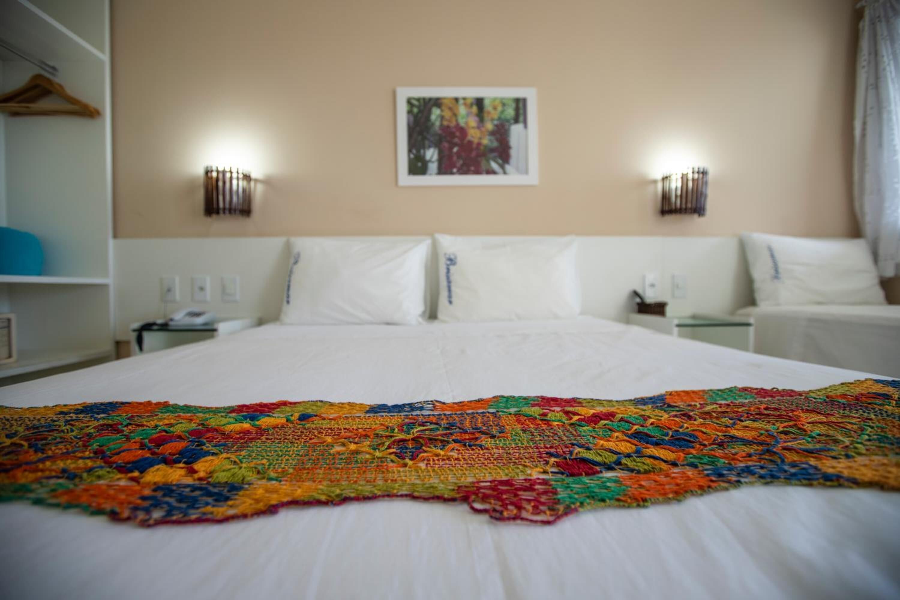 Een hotelkamer met een groot bed, een kleurrijk dekbed, twee nachtkastjes, een wandlamp en een schilderij aan de muur.