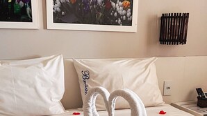 A hotel room with a bed, white pillows, a heart-shaped towel arrangement, and two framed floral pictures on the wall. - Brisamar Hotel Pousada (Barra de São Miguel)