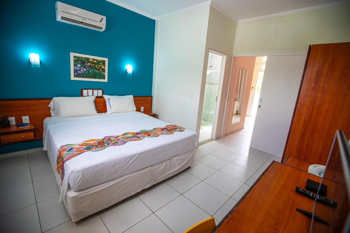 A hotel room with a bed, bedside tables, an air conditioner, a framed picture, and a door leading to a bathroom.