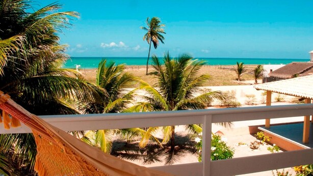 A balcony with a view of a beach, palm trees, and a clear blue sky. - Brisamar Hotel Pousada (Barra de São Miguel)
