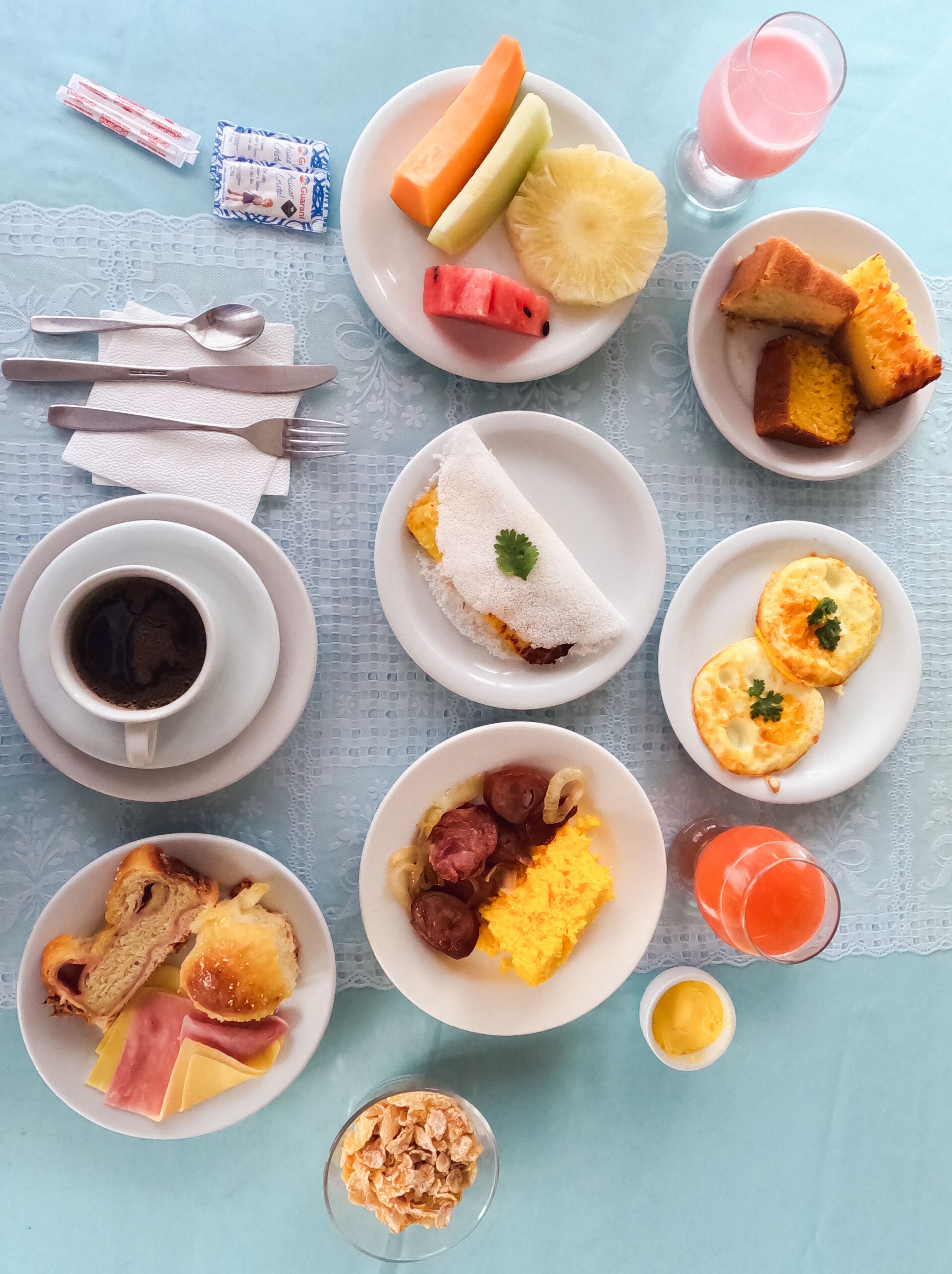 Une table dressée avec divers aliments pour le petit-déjeuner, notamment des fruits, du pain, des œufs et des boissons.