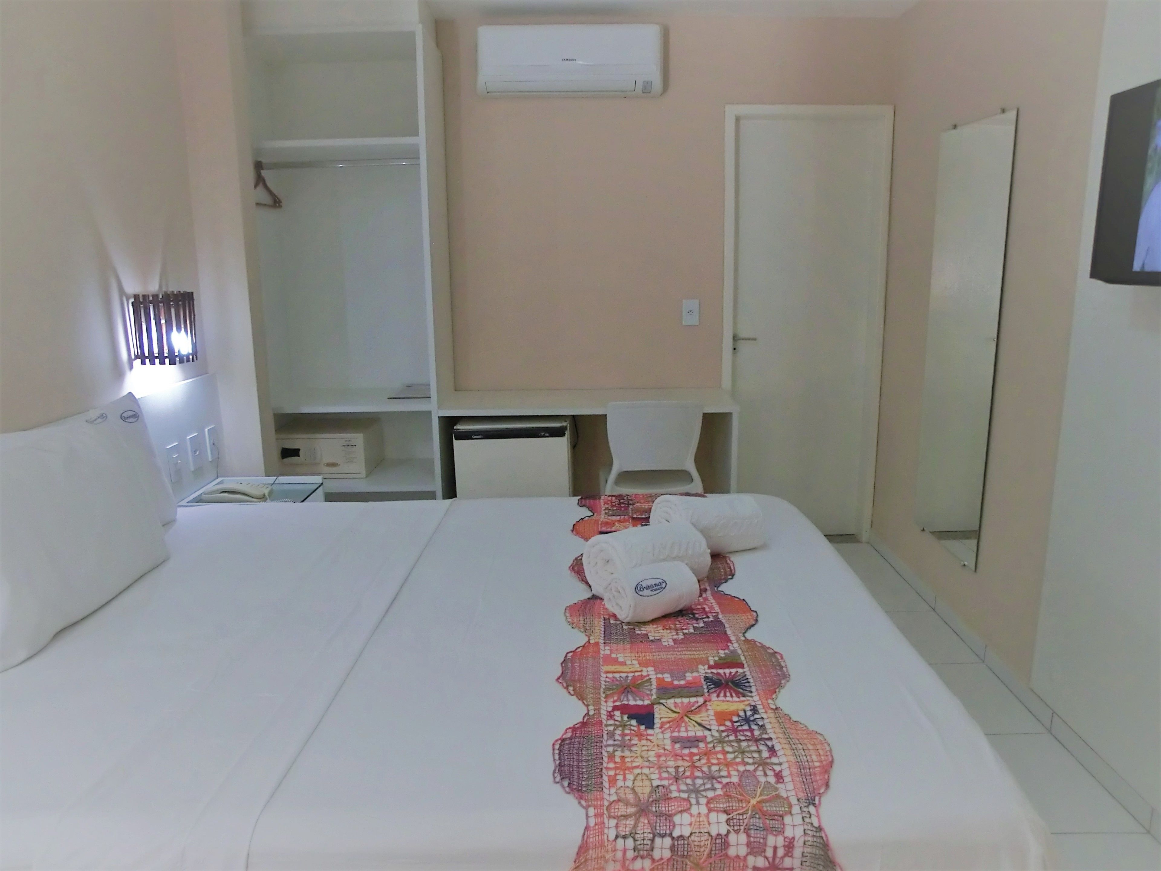 A hotel room with a bed, a desk, a chair, a wardrobe, and a mirror.