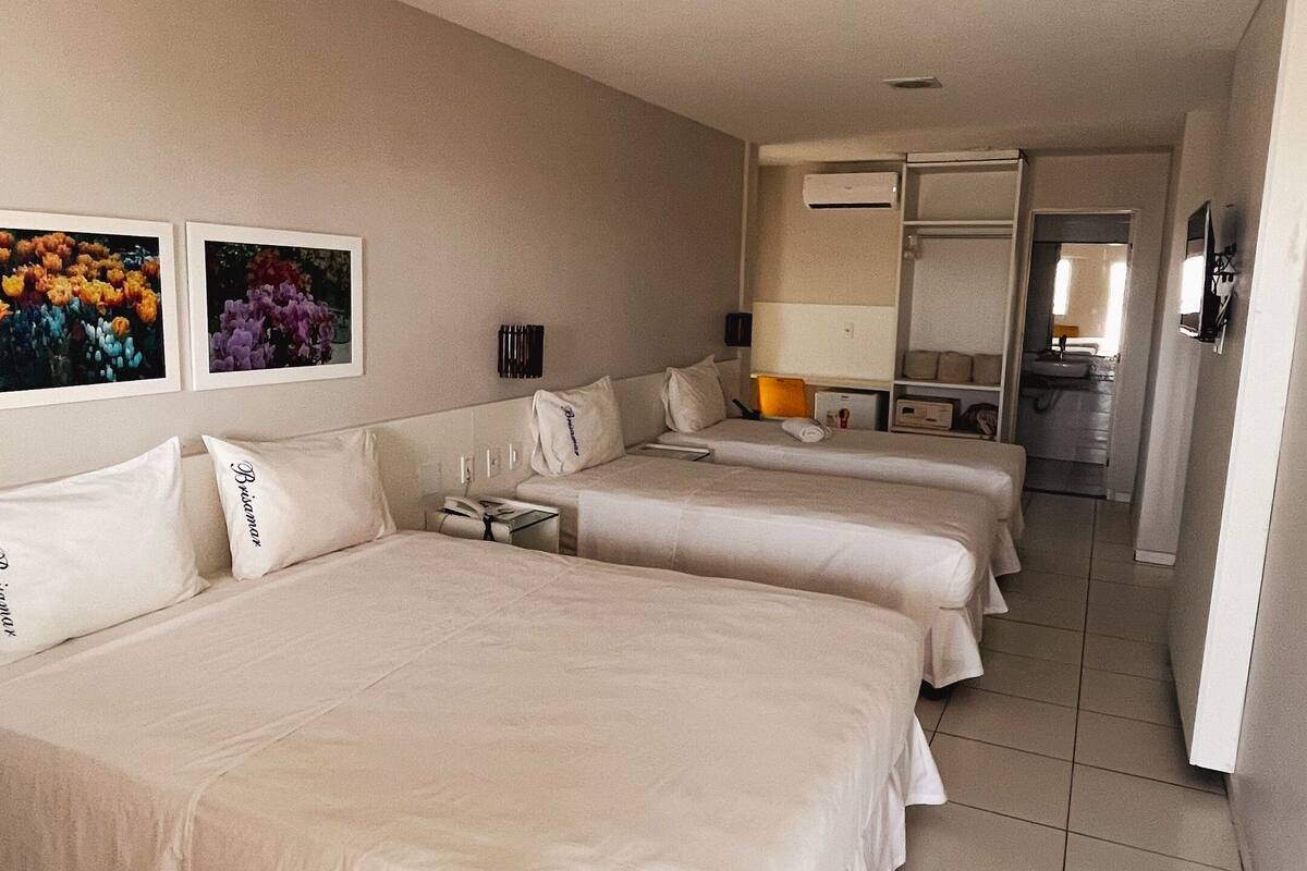 A hotel room with three beds, a desk, and a bathroom visible in the background.