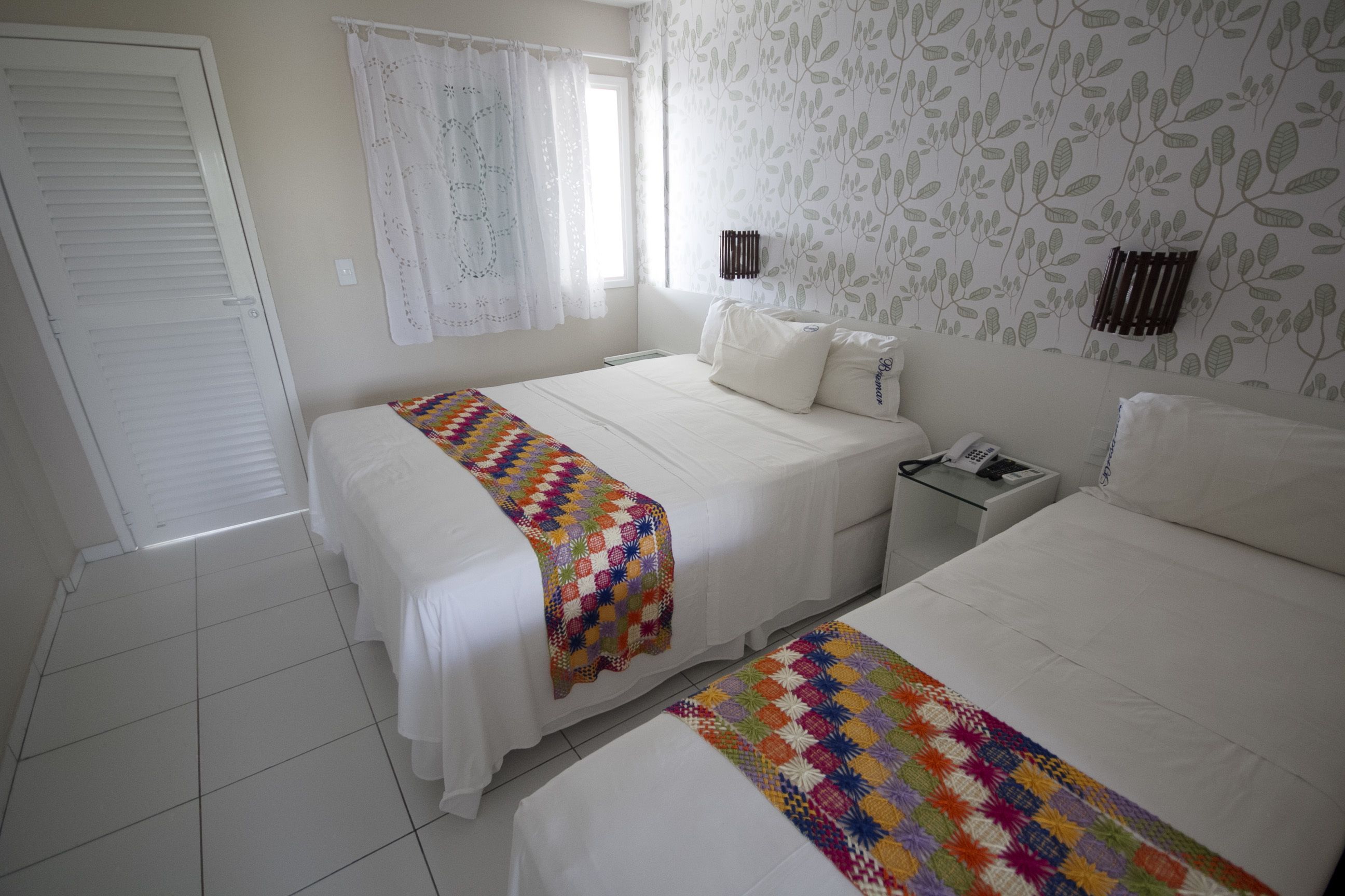 A hotel room with two beds, a bedside table with a phone, and a window with curtains.