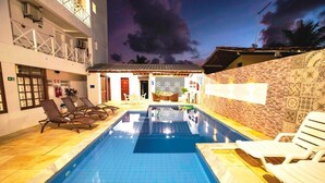 A swimming pool with lounge chairs, a covered seating area, and a building with patterned walls. - Brisamar Hotel Pousada (Barra de São Miguel)