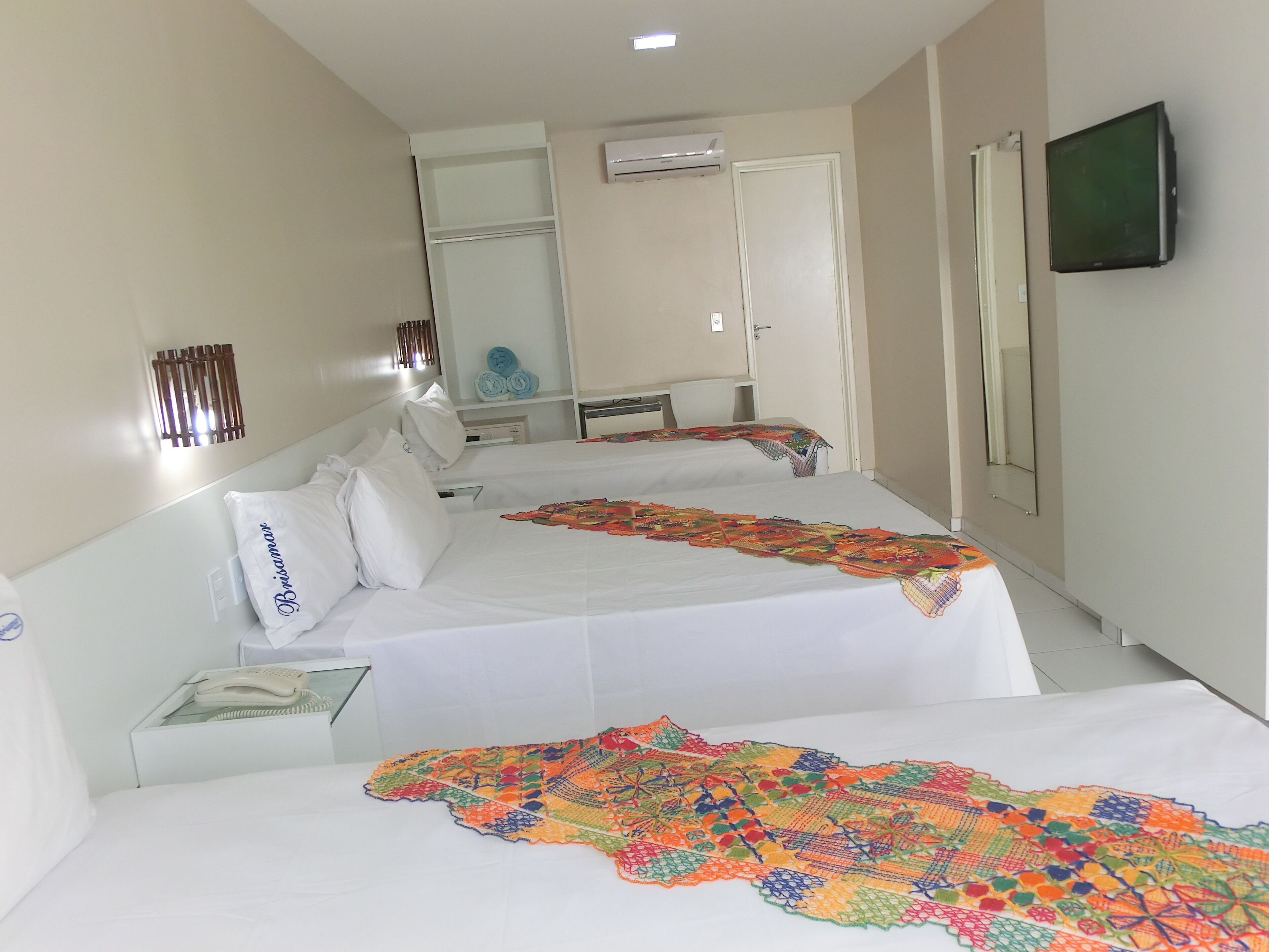 Habitación de hotel con dos camas, un televisor montado en la pared y una puerta que da a un baño.