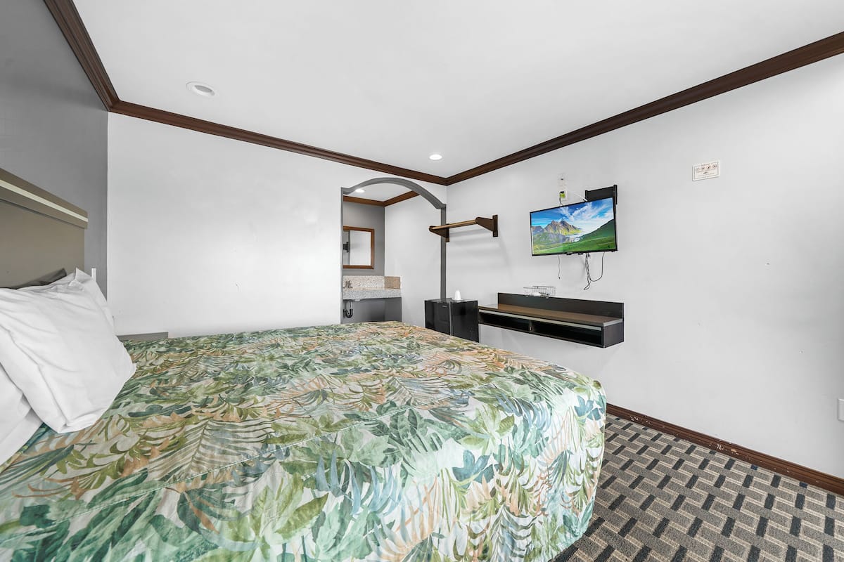 Ein Hotelzimmer mit Bett, Wandfernseher, kleinem Schreibtisch und Spiegel.