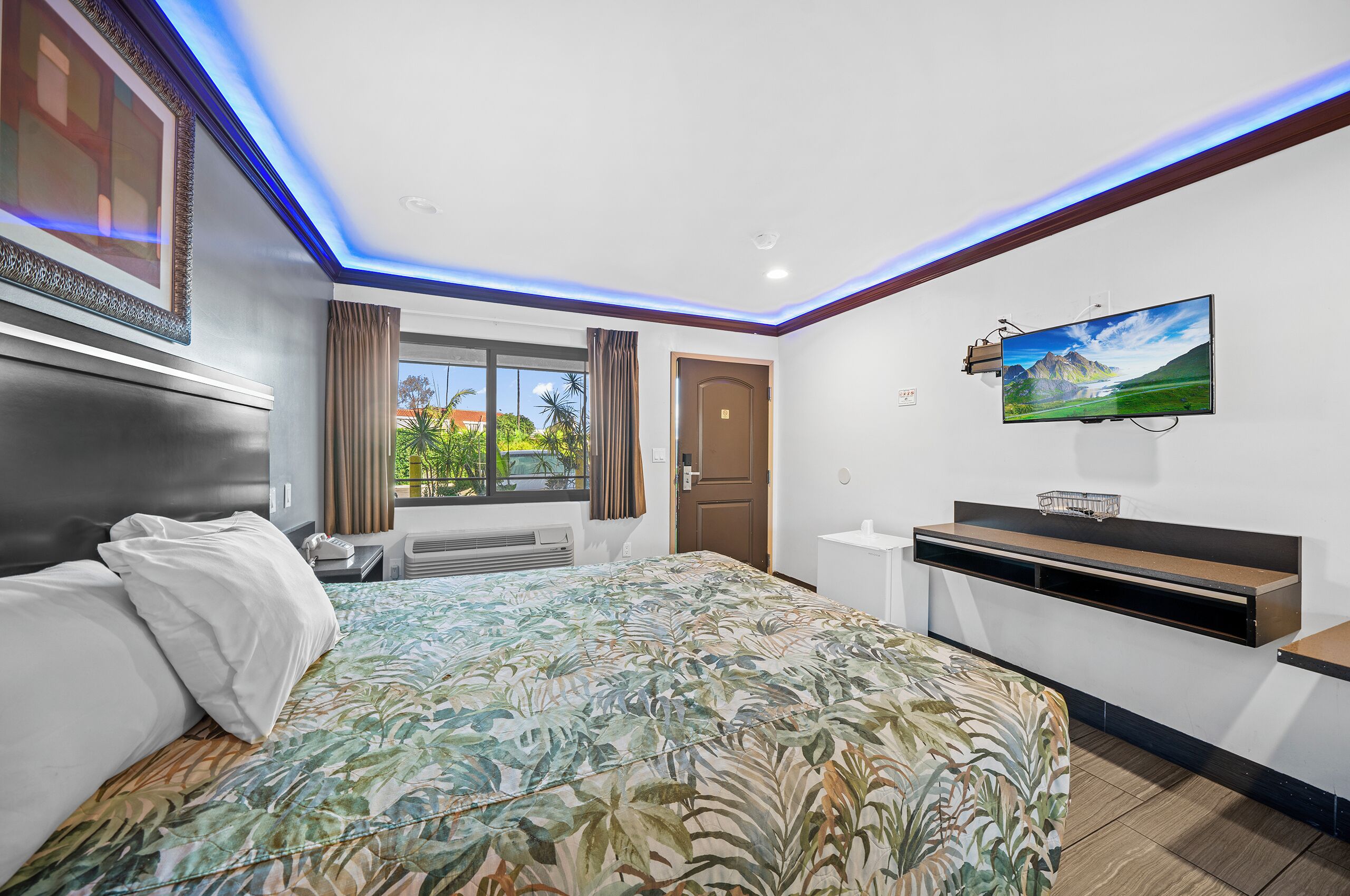 A modern hotel room with a large bed, a flat-screen TV, a desk, and a window with curtains.
