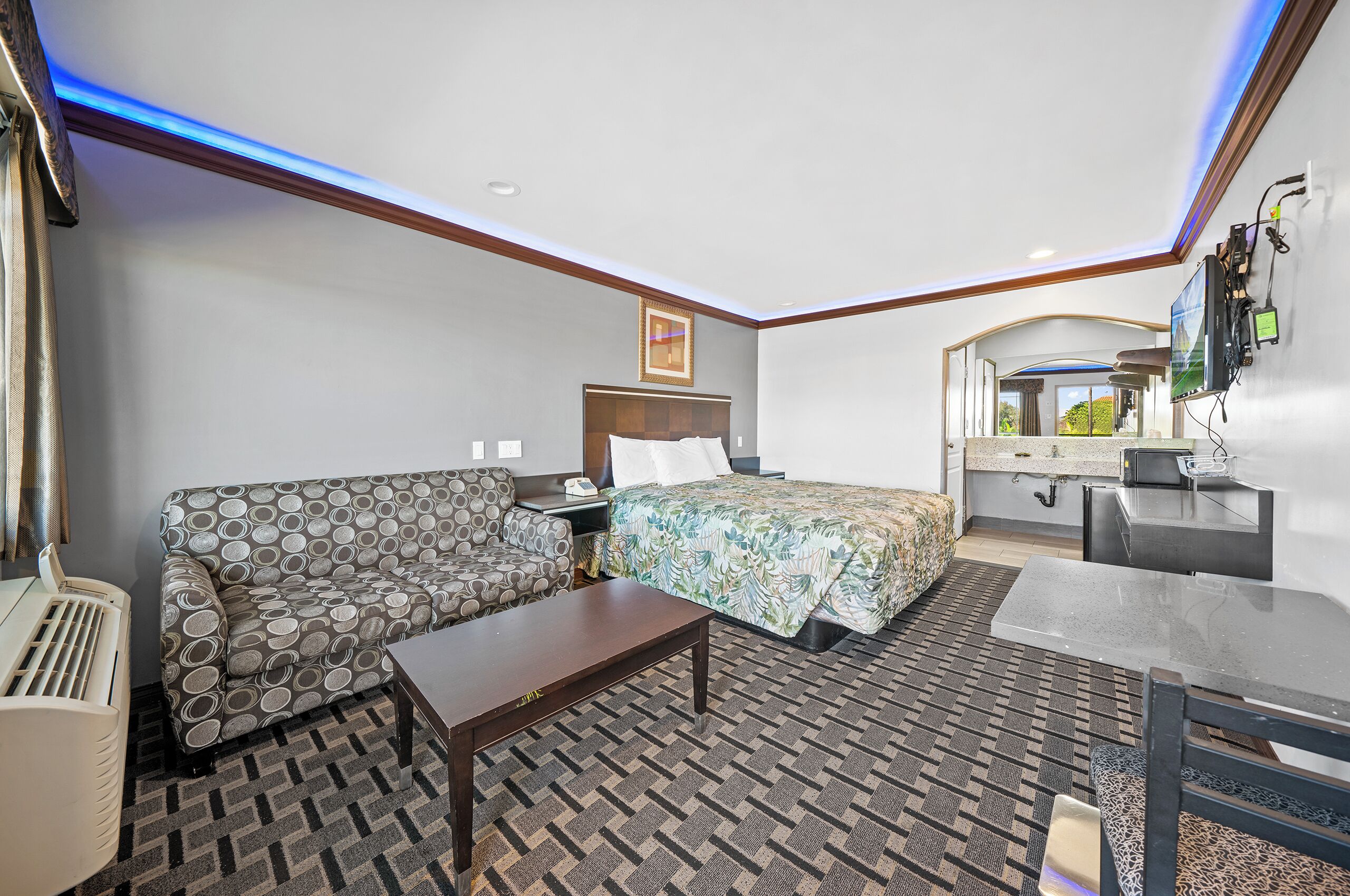A hotel room with a bed, sofa, table, and a small kitchenette.