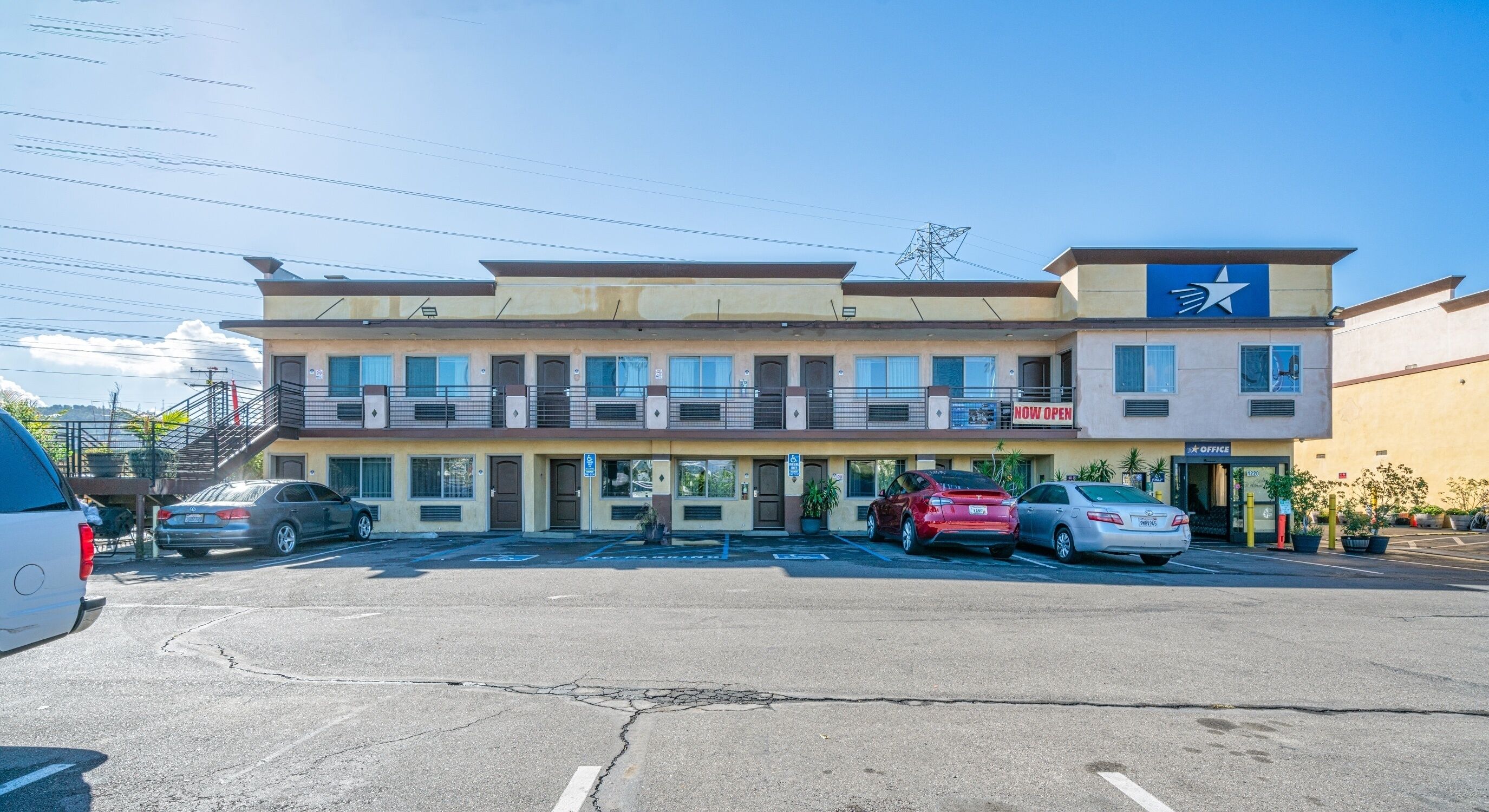 A two-story building with a parking lot in front. There are several cars parked, and the building has a sign that says "NOW OPEN".
