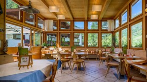 A restaurant with wooden interiors, large windows, and multiple tables and chairs. - Wellness- und Genußhotel Rosmarie (Moso in Passiria)