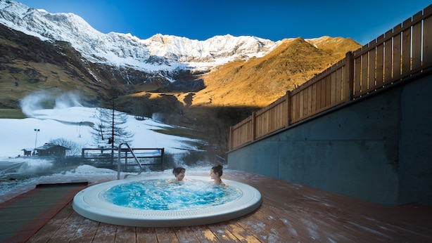 A hot tub with two people, surrounded by a wooden deck and a mountain backdrop. - Wellness- und Genußhotel Rosmarie (Moso in Passiria)