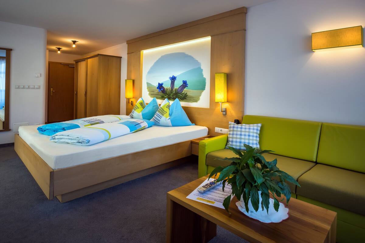 A hotel room with a bed, a green sofa, a wooden coffee table, and a wall-mounted painting.