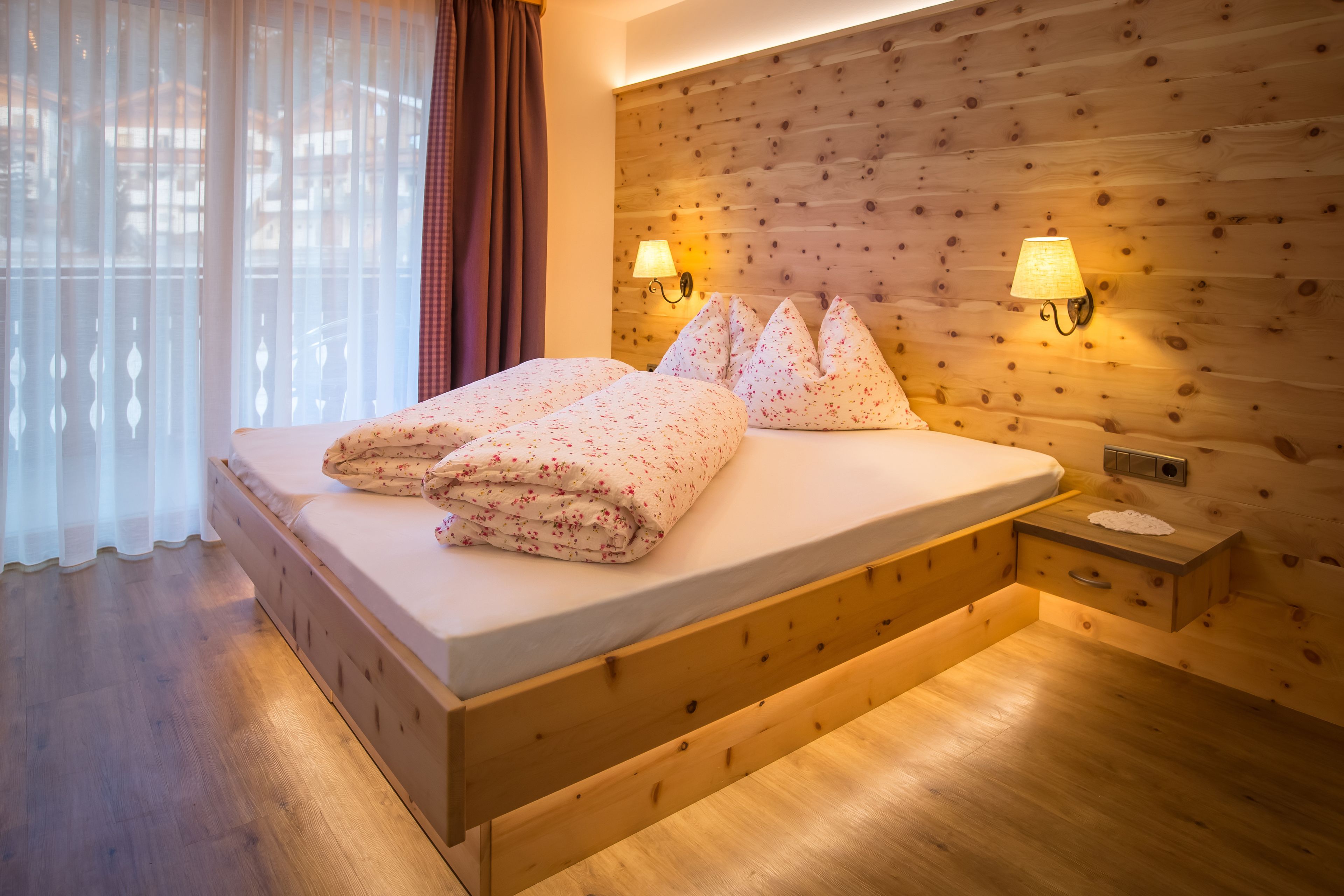 A wooden bed with a headboard, two bedside lamps, and a nightstand with a lamp.