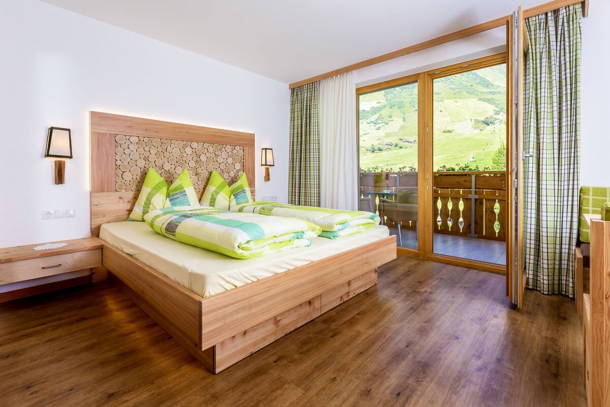 A bedroom with a wooden bed, a nightstand, a wall-mounted lamp, and a large sliding glass door leading to a balcony.