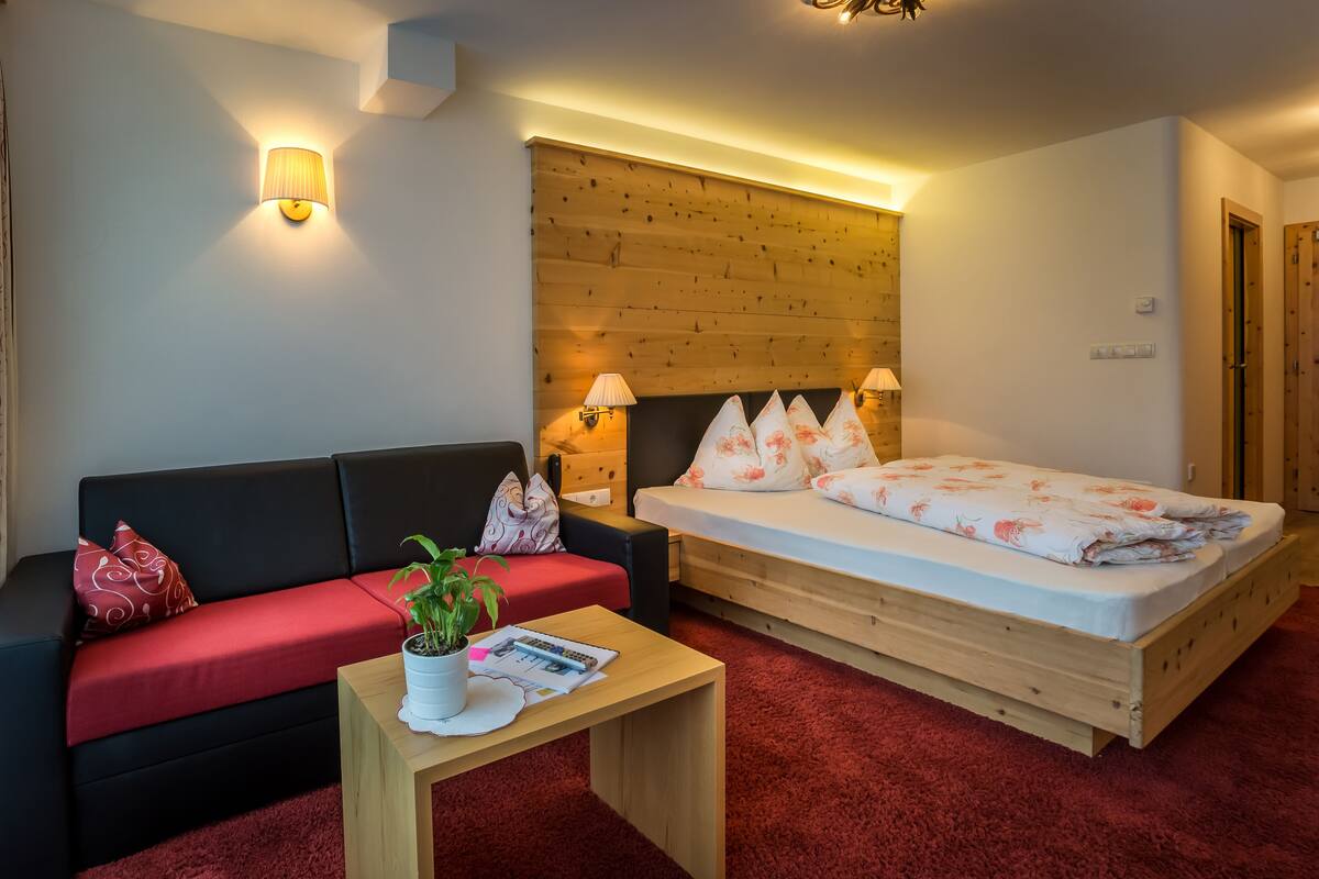 A modern room with a wooden headboard bed, a red sofa, a wooden coffee table, and a small plant.