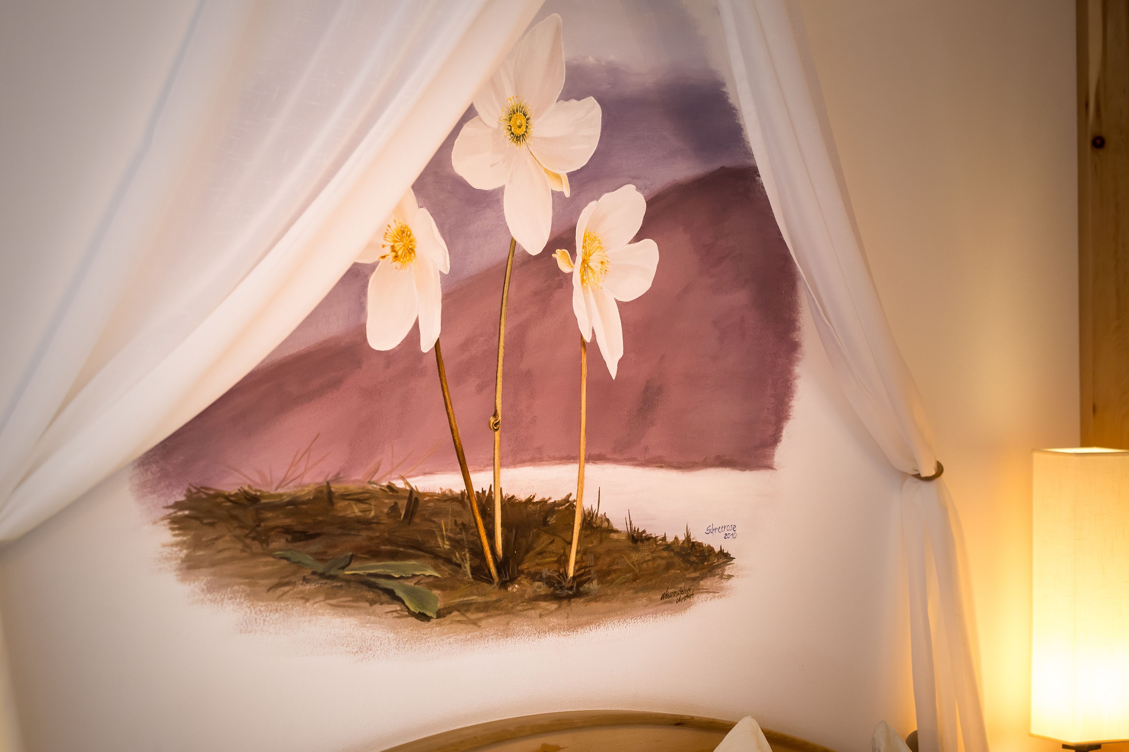 A wall with a painted flower arrangement and a lamp.