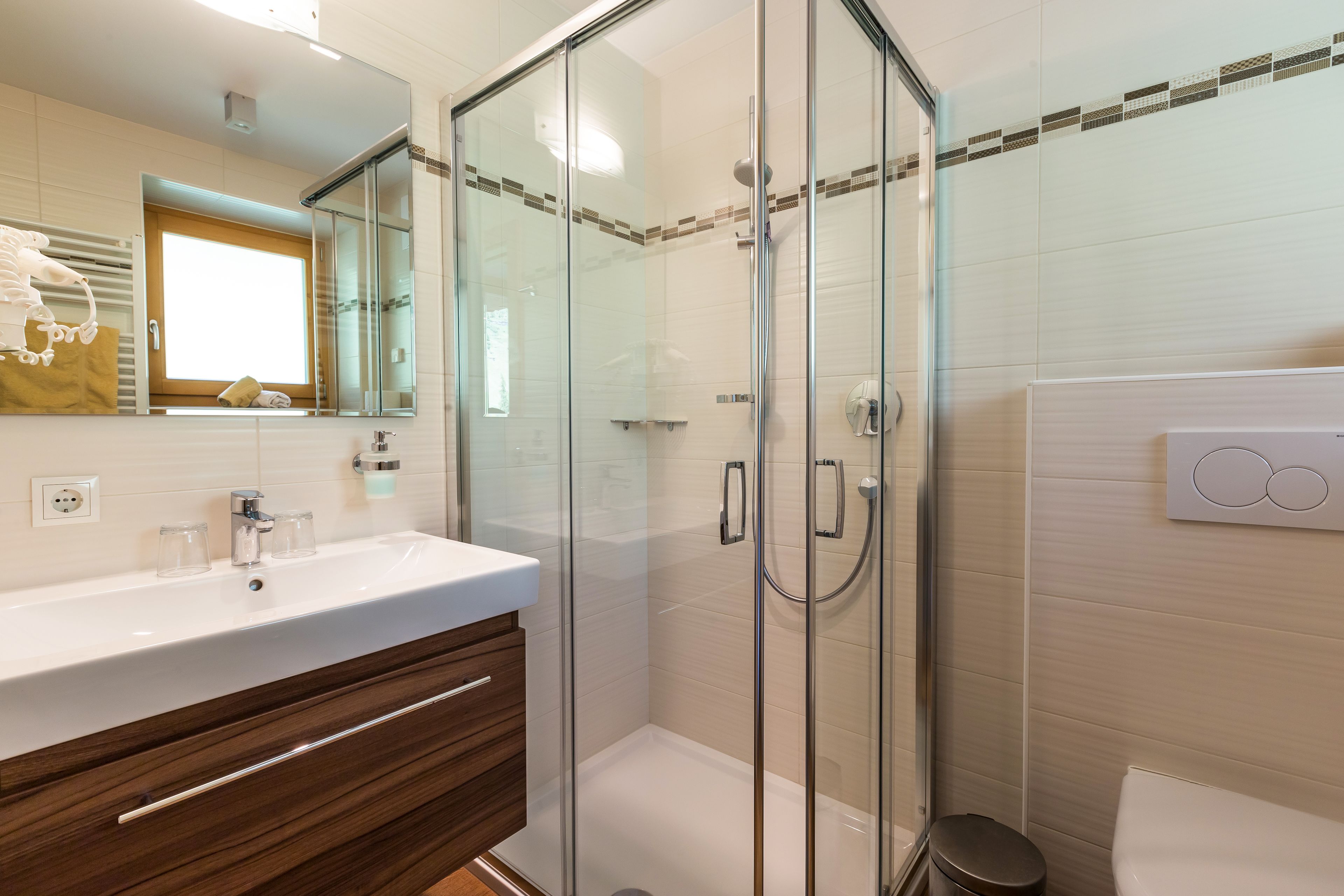 Een moderne badkamer met een douchecabine van glas, een wit wastafelmeubel met een houten kast en een toilet.
