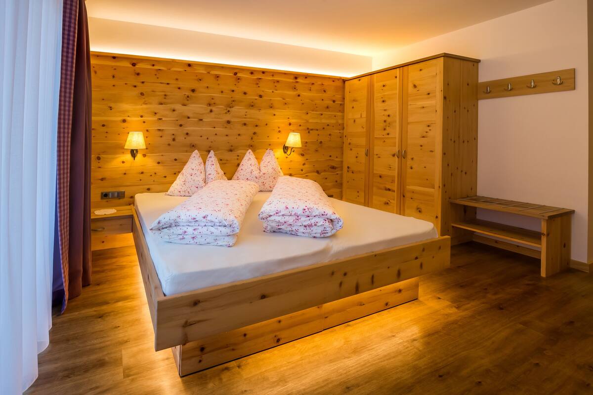 A wooden-paneled bedroom with a bed, bedside lamps, and a wooden wardrobe.