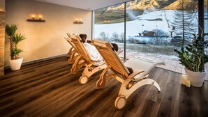 A spa room with wooden loungers, a large window with a snowy mountain view, and potted plants. - Wellness- und Genußhotel Rosmarie (Moso in Passiria)