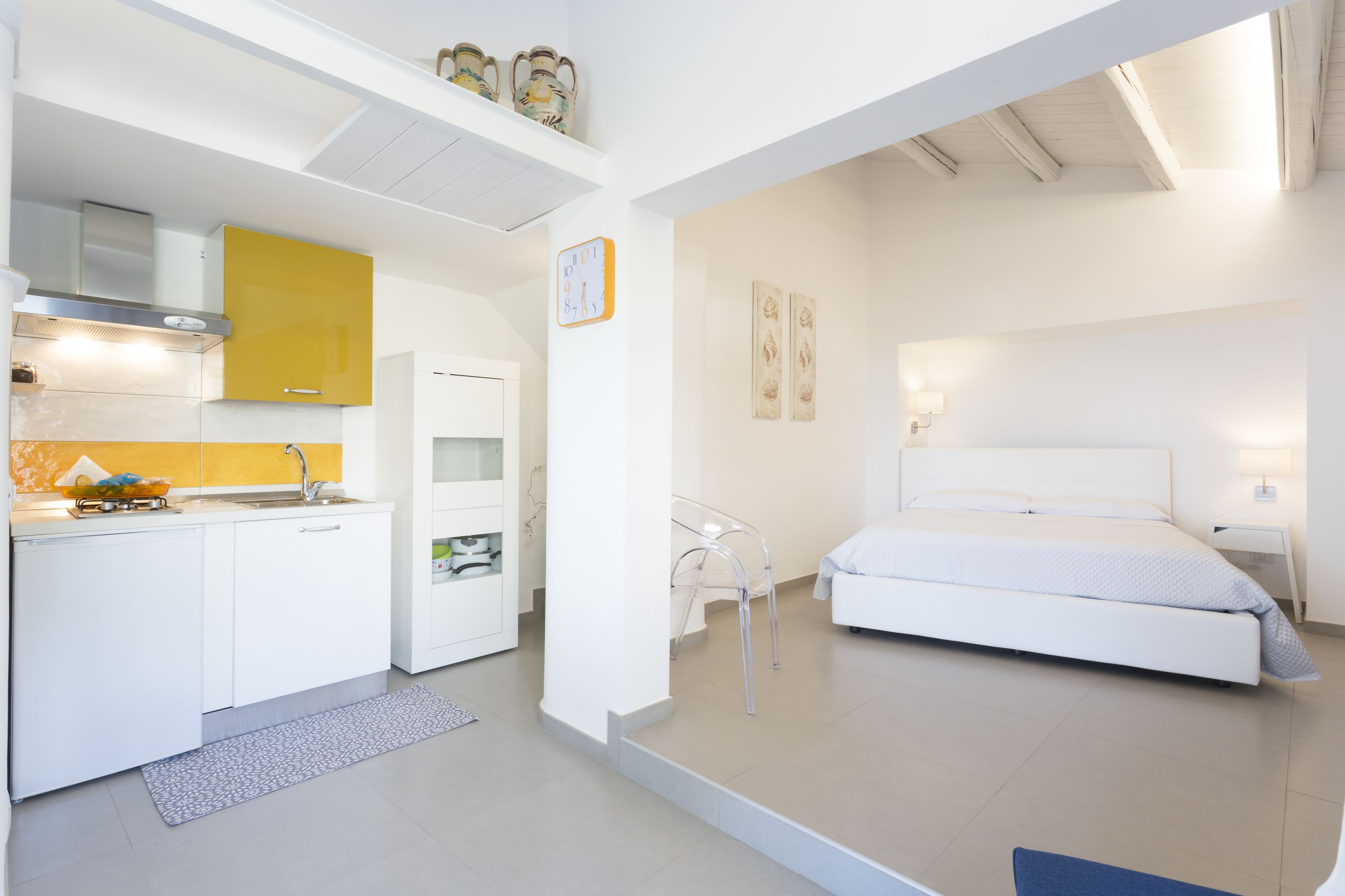 Een moderne, goed verlichte kamer met een bed, een kleine kitchenette en een transparante glazen stoel.