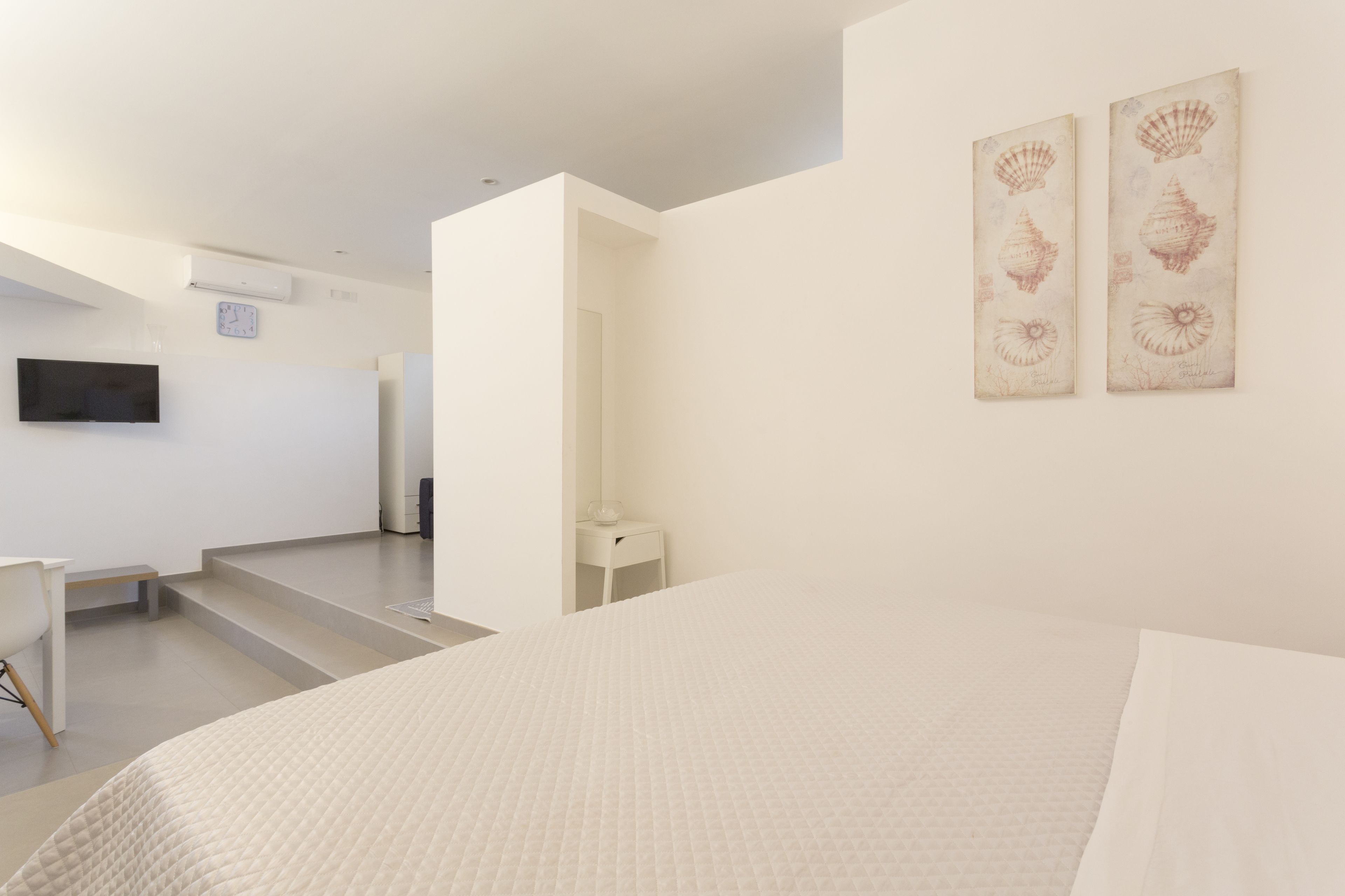 A modern hotel room with a bed, a desk, a chair, and two wall-mounted artworks.