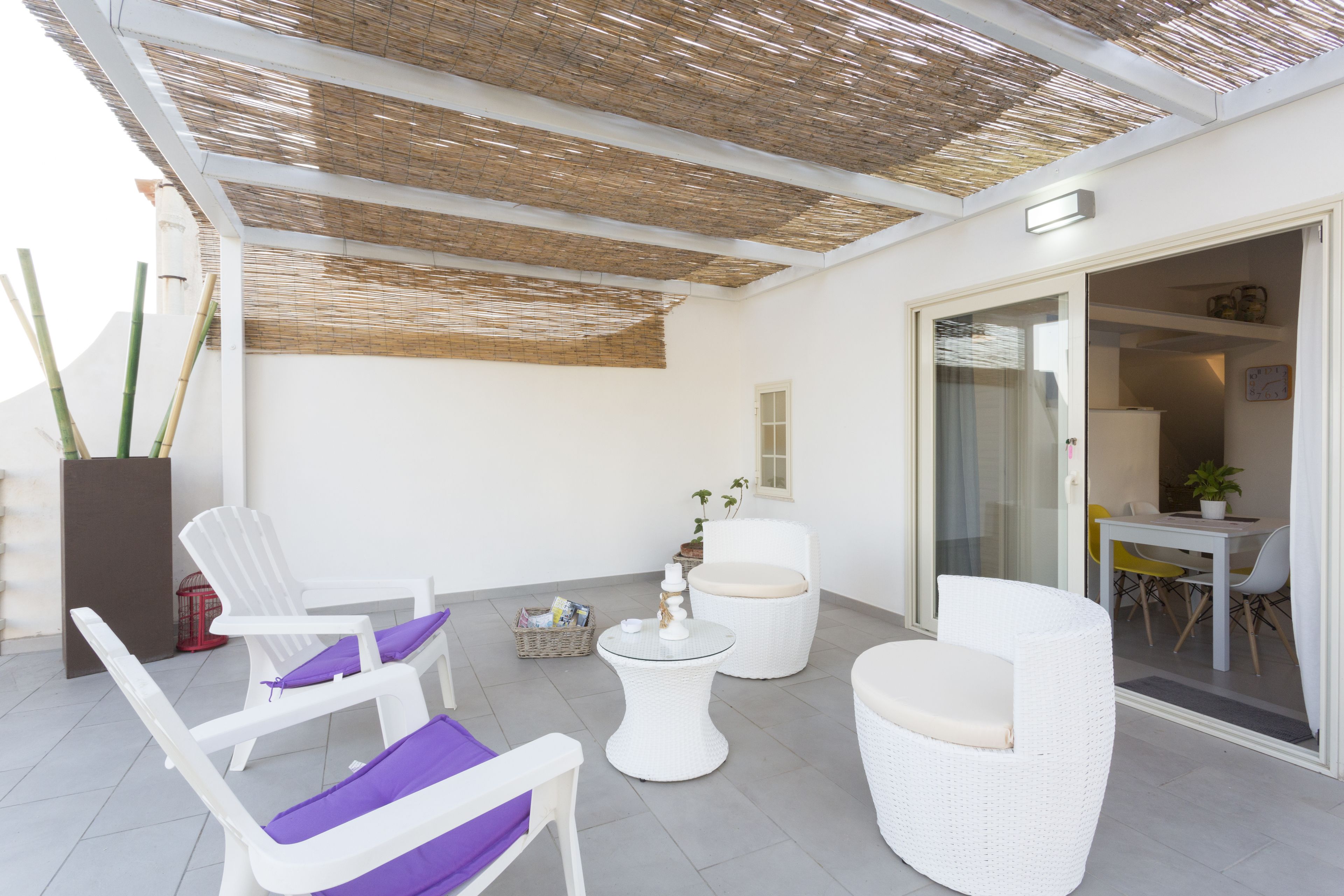 Un espace extérieur aménagé, abrité et doté de mobilier en osier blanc et d’une table en verre.