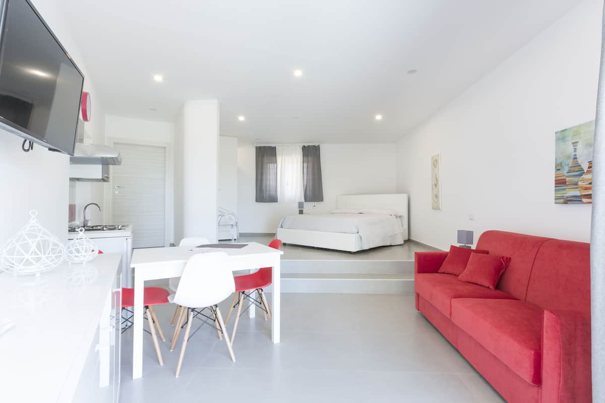 A modern, well-lit room with a dining area, a bed, and a red sofa.