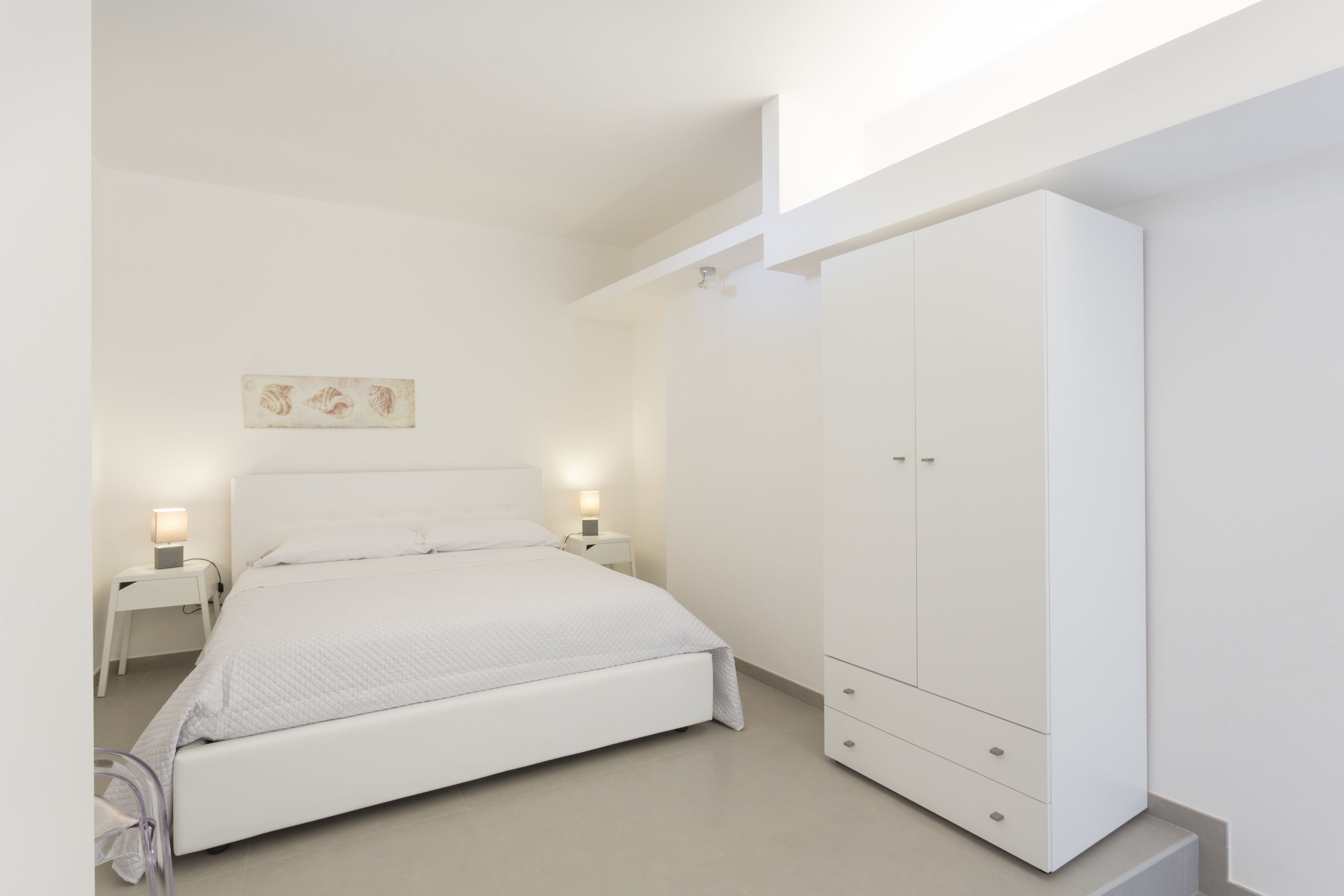 A bedroom with a bed, nightstands, a wardrobe, and a wall-mounted artwork.