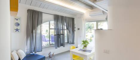 A modern room with a bed, a dining table with chairs, a window with curtains, and a plant on the table.