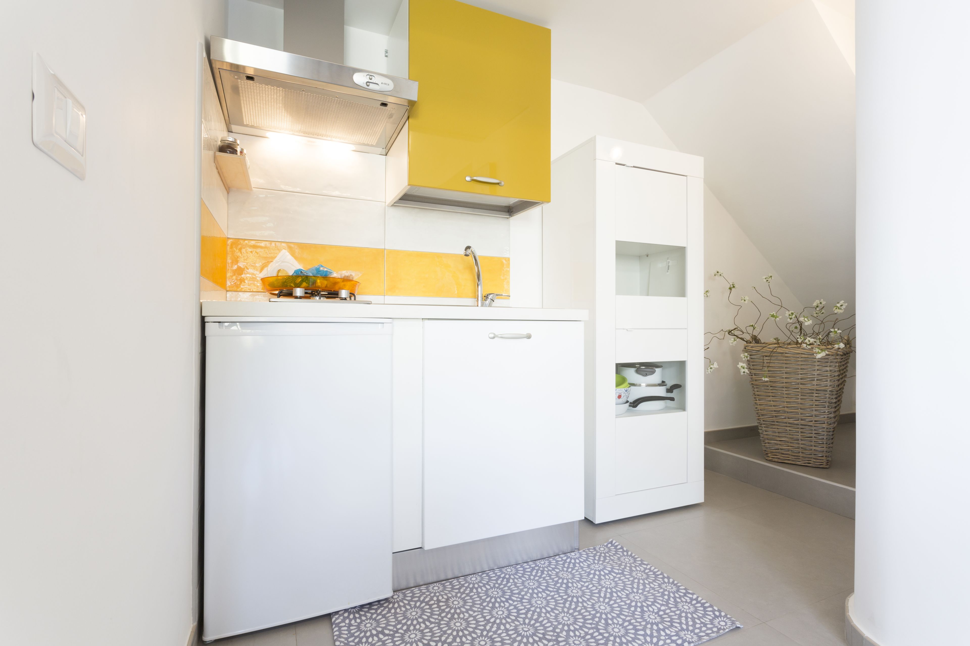 Een kleine keuken met witte kasten, een gele accentmuur en een ingebouwd spoelgedeelte.