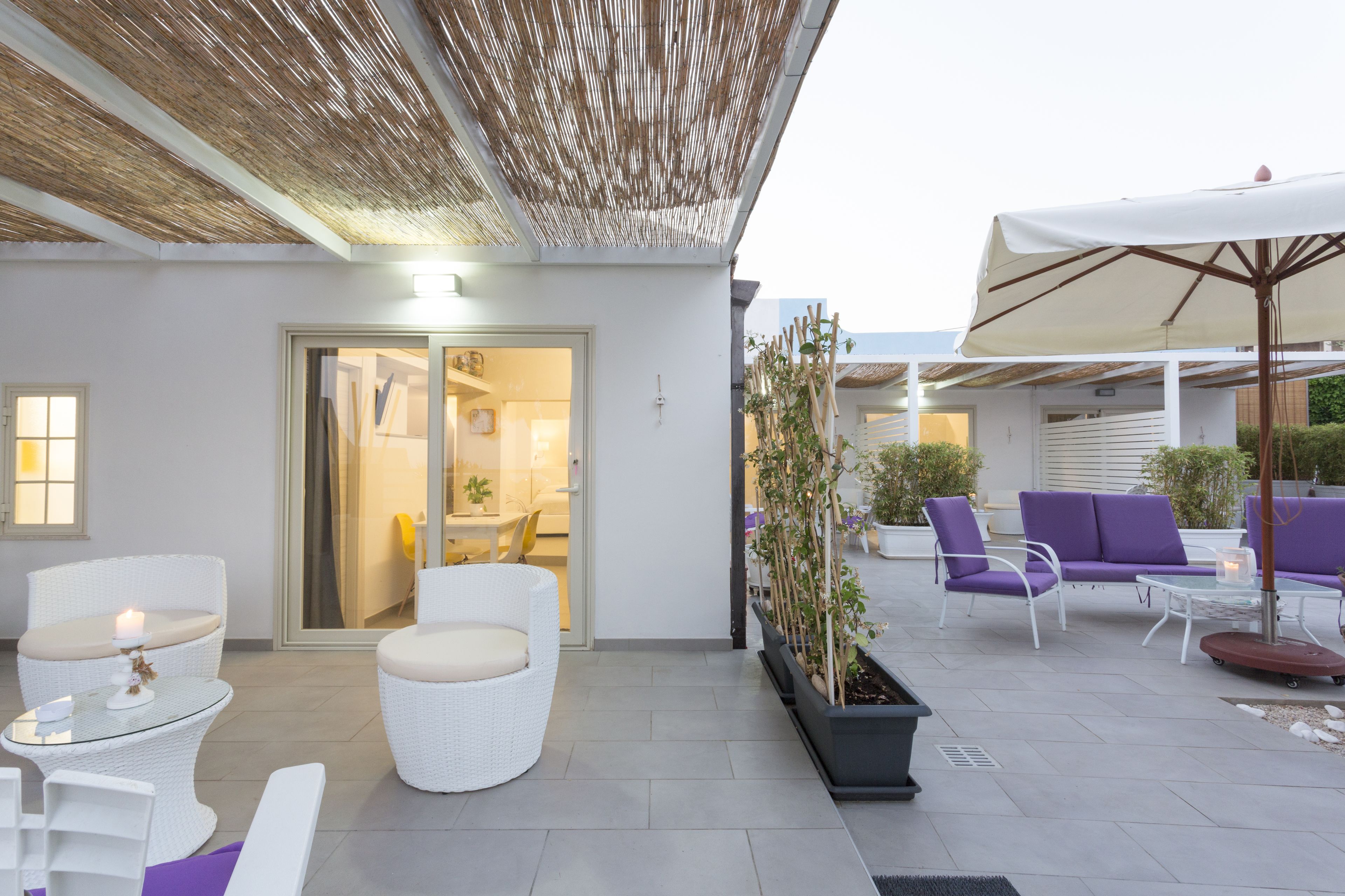 Une terrasse extérieure moderne, dotée de meubles en osier, d’une table en verre et d’un espace salon avec des coussins.