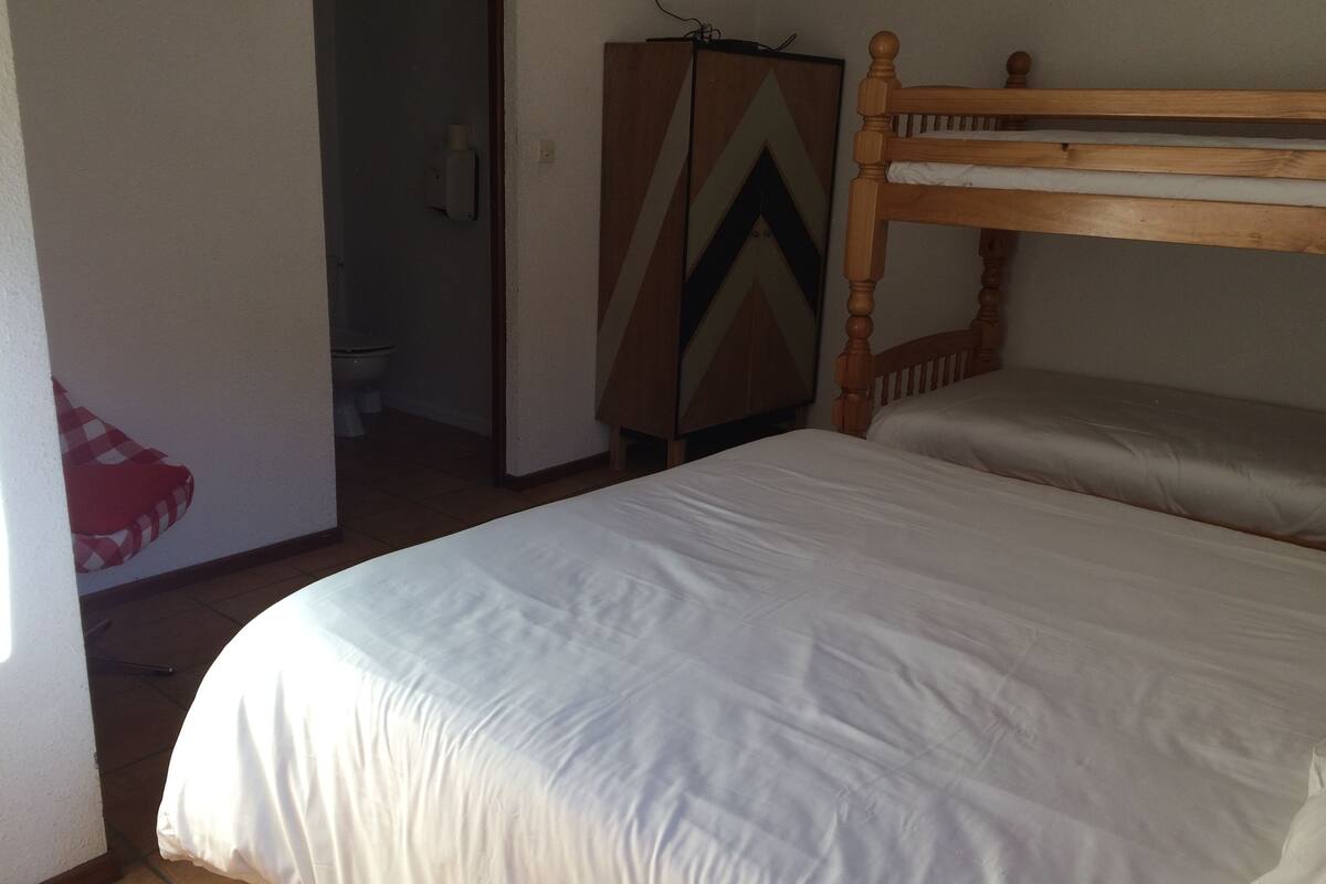 A bedroom with a wooden bed frame, a wardrobe, and a bathroom visible through an open door.